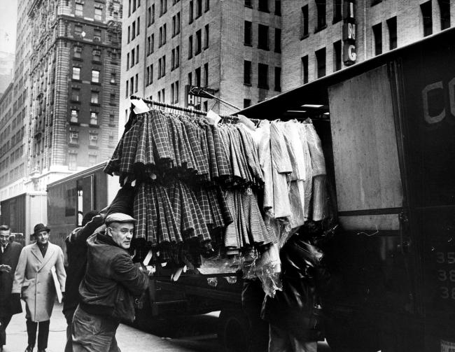 Black and white image of a man pushing a full garment rack on the sidewalk